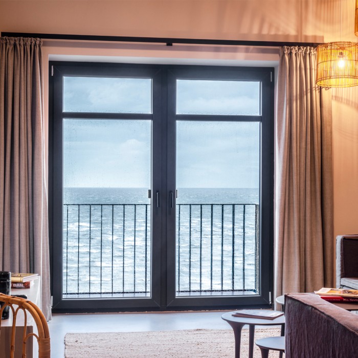 Ferestre-Taq-Veka-Fereastră modernă de balcon cu două uși, rame negre și vedere la mare, cu perdele elegante și un interior minimalist.