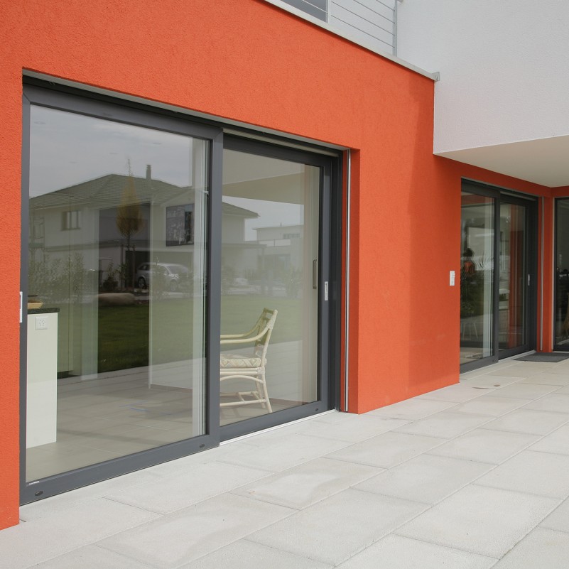 Taq-Usi pvc-Usi-Vekamotion -82-Ușă glisantă modernă cu cadru gri și perete exterior portocaliu, design elegant pentru accesul luminos către grădină.